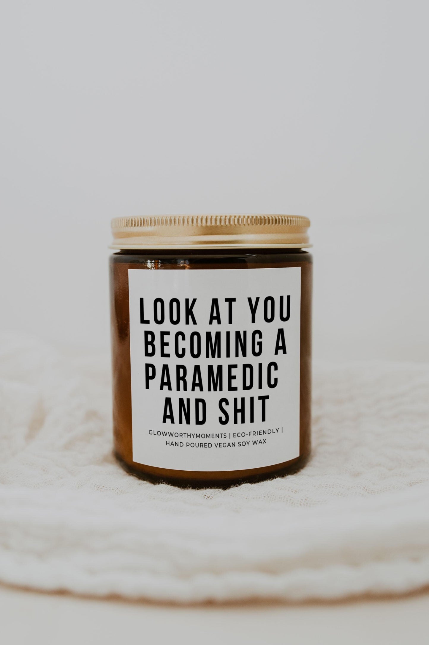 EMT graduate holding candle with 'Look at you becoming a paramedic' quote
