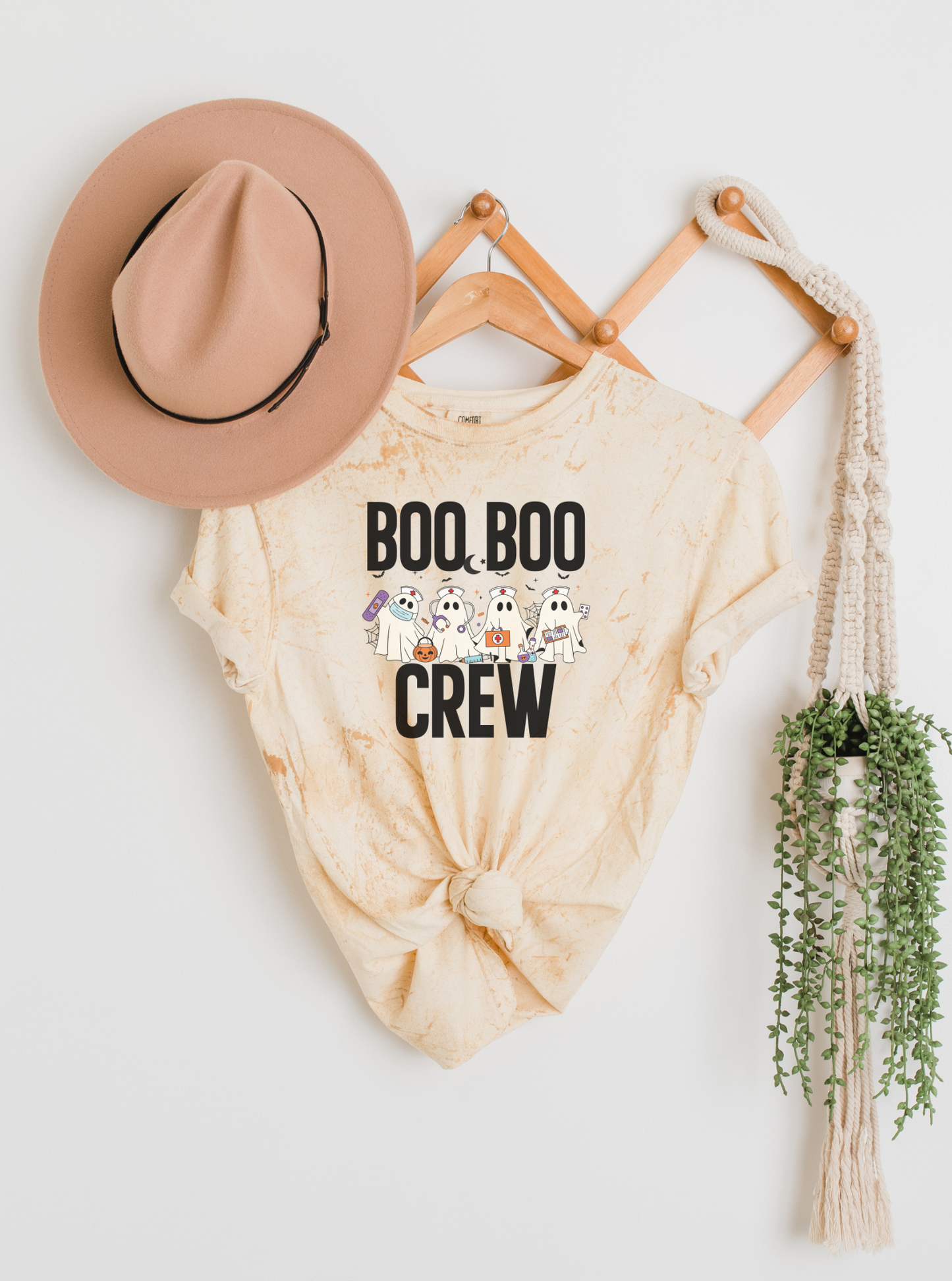 Beige t-shirt with 'BOO BOO CREW' text, beige hat, and decorative items on a white background
