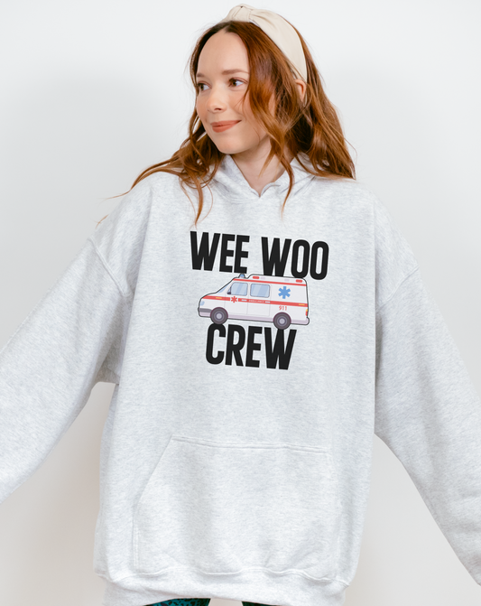 Person wearing a gray hoodie with 'WEE WOO CREW' text and ambulance graphic on a white background