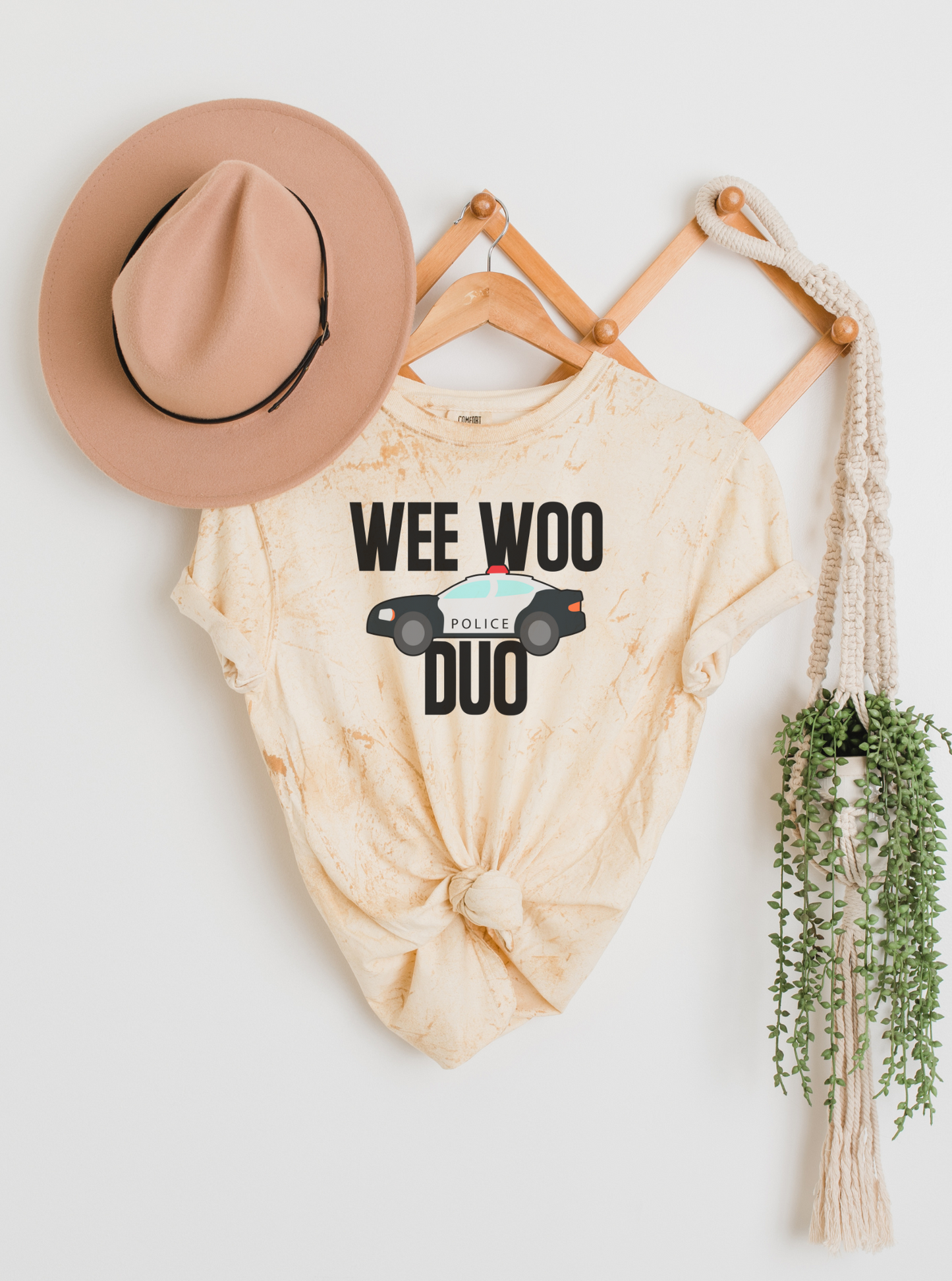 Beige tie-dye shirt with 'WEE WOO DUO' text, hat, and plant on a white background