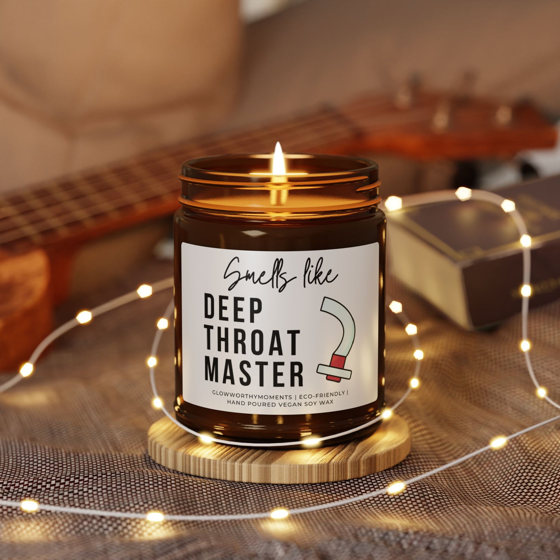 Candle in a jar with a humorous label on a wooden coaster, surrounded by string lights and a guitar in the background.