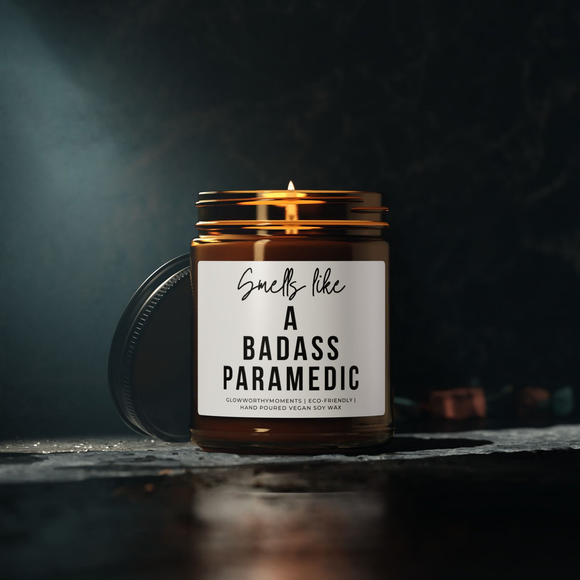 Candle in a jar with a label reading 'Smells like a badass paramedic' on a dark background.