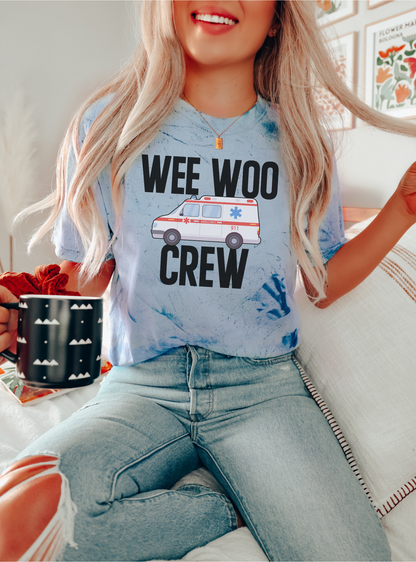 Person wearing a blue t-shirt with 'WEE WOO CREW' text and an ambulance graphic, sitting indoors.