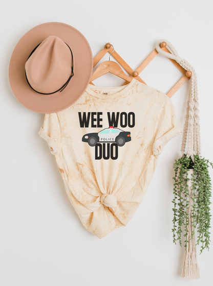 Beige tie-dye shirt with 'WEE WOO DUO' text, hat, and plant on a white background