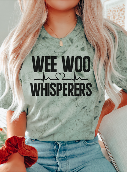 Person wearing a shirt with 'WEE WOO WHISPERERS' text and heartbeat design.